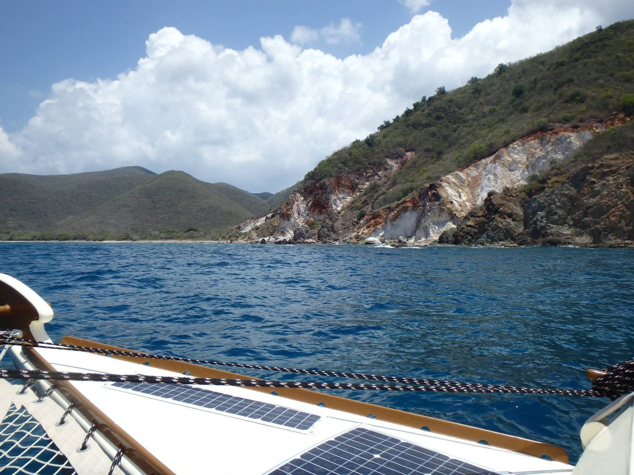 View from the Mahiya bow over solar panels toward dramatic colorful rocky VI cliffs and deep blue water