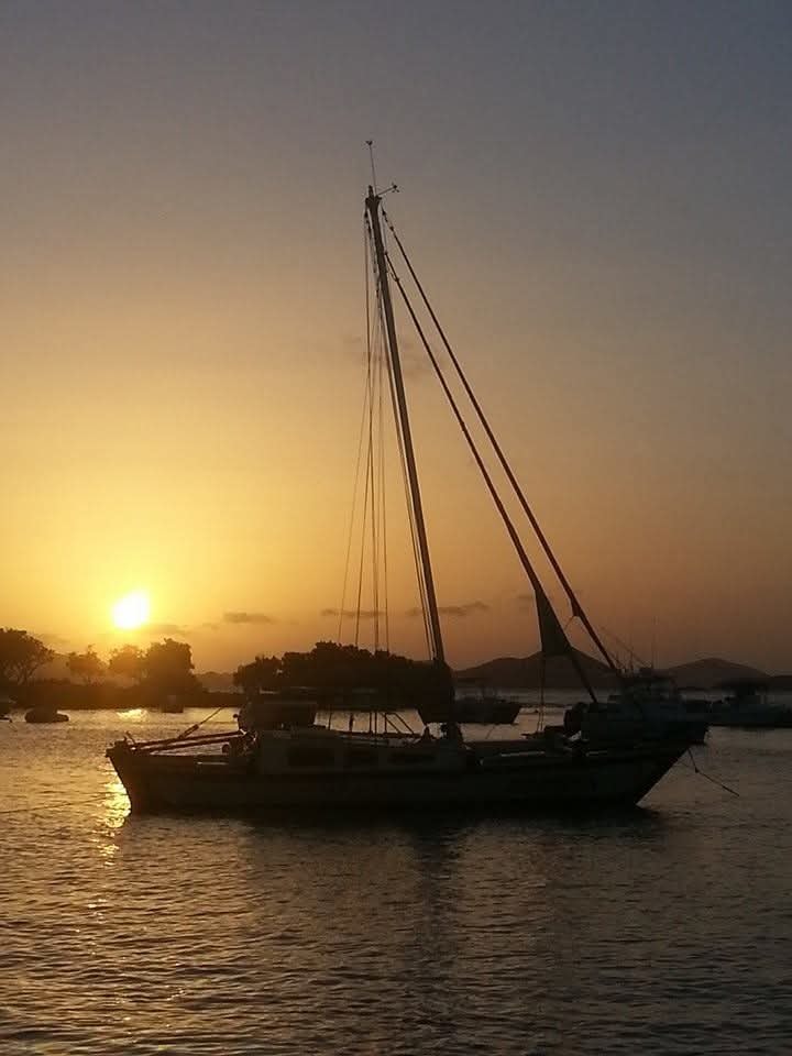 Sailboat silhouetted against a stunning golden sunset over a calm harbor with VI island mountains behind