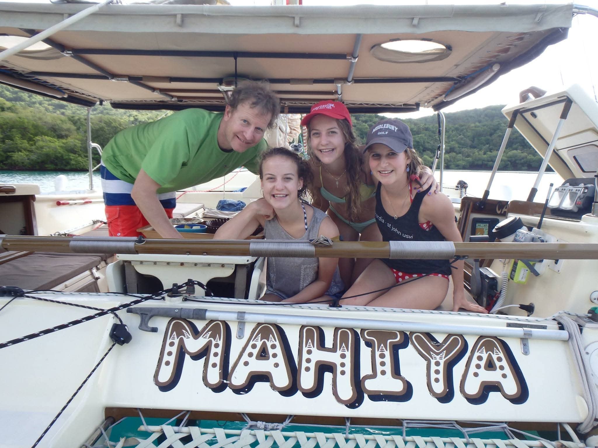 Happy group of four guests posing behind the MAHIYA name on the stern, lush green VI cove behind
