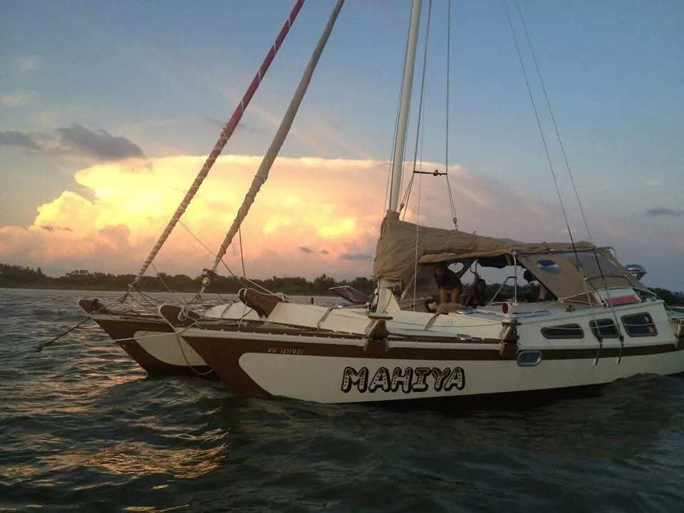 The Mahiya catamaran moored at dusk with MAHIYA name on the hull, dramatic golden and purple storm clouds behind, trees silhouetted