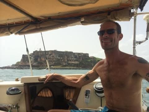 Captain Karl smiling at the helm of the Mahiya with El Morro fortress visible behind him in the harbor