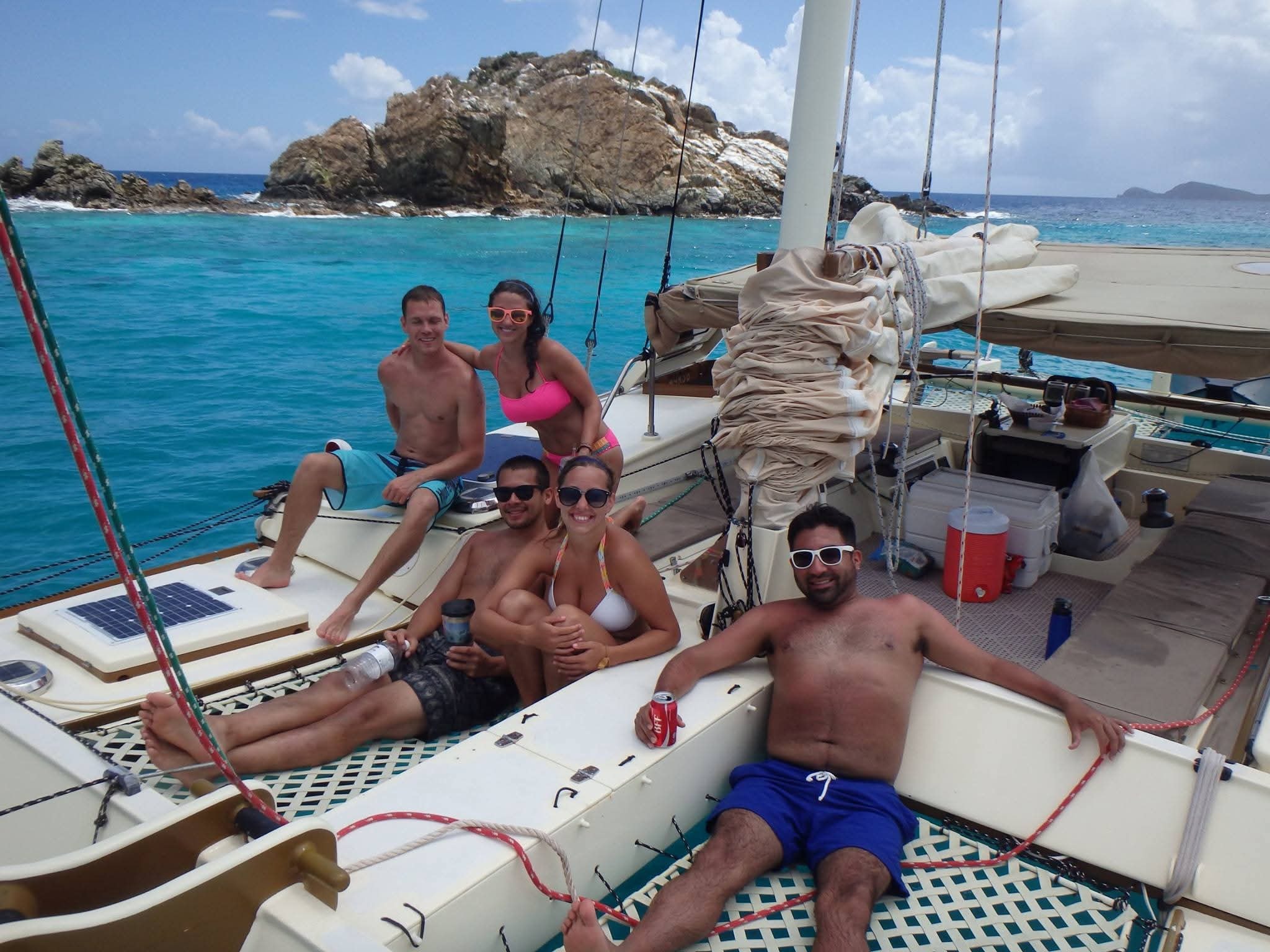 Happy group of five guests lounging on the Mahiya catamaran deck with brilliant turquoise water and a rocky island behind