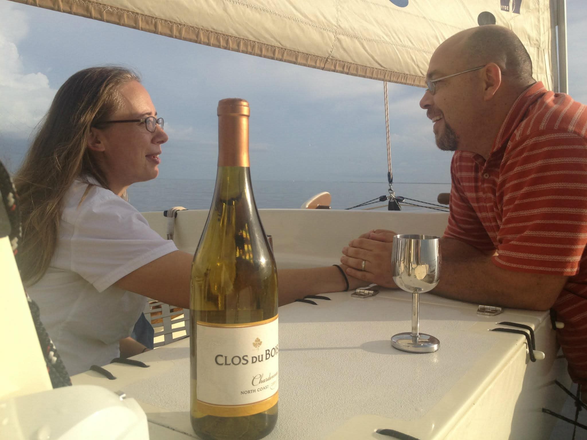 Couple sharing wine aboard the Mahiya at sunset, bottle of Clos du Bois Chardonnay on the table, open ocean behind