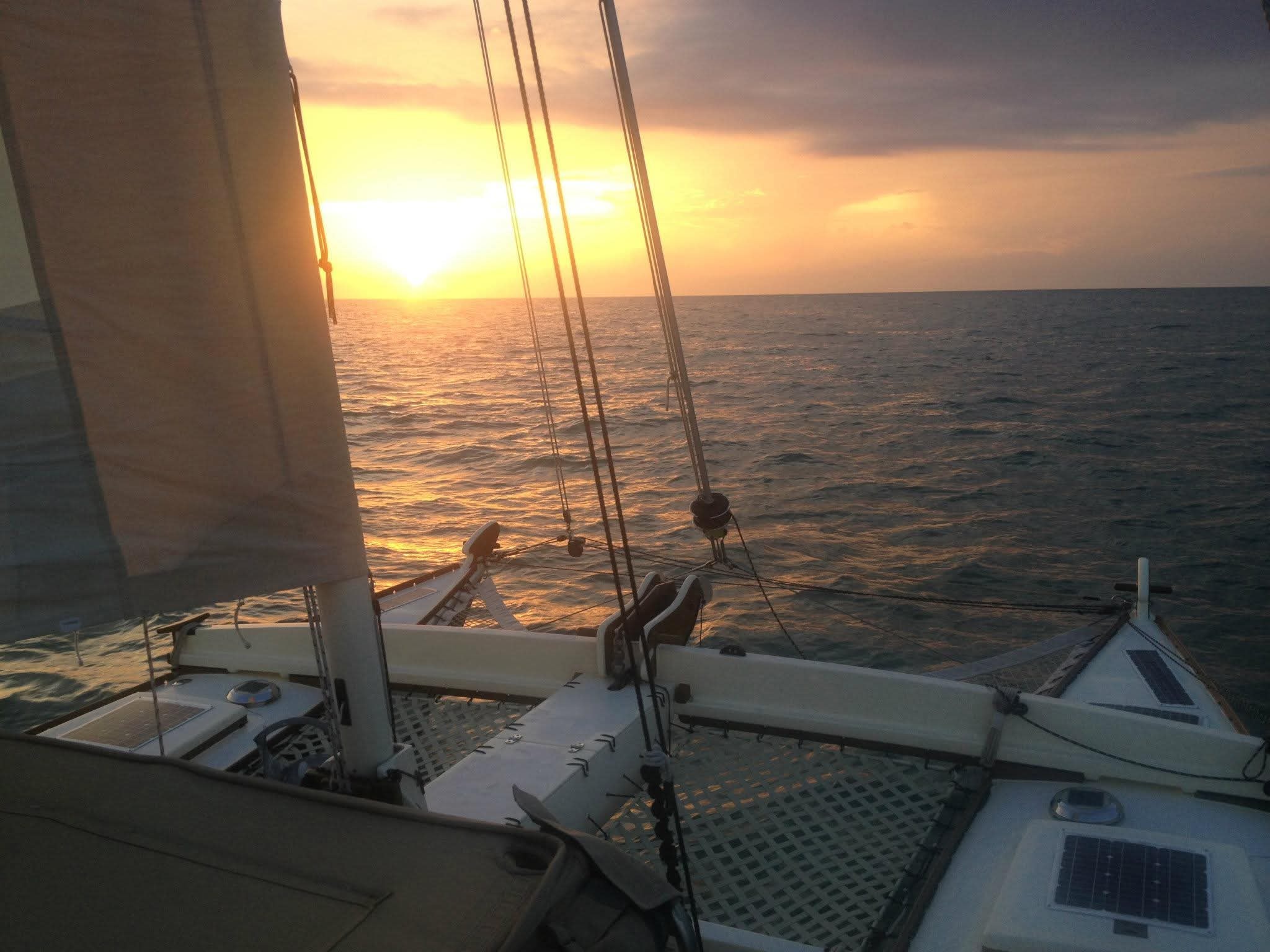 Golden sunset from the Mahiya deck looking forward past the sail and rigging over a calm open ocean