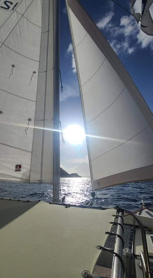 Looking up through the Mahiya sails with sun flare and island silhouette