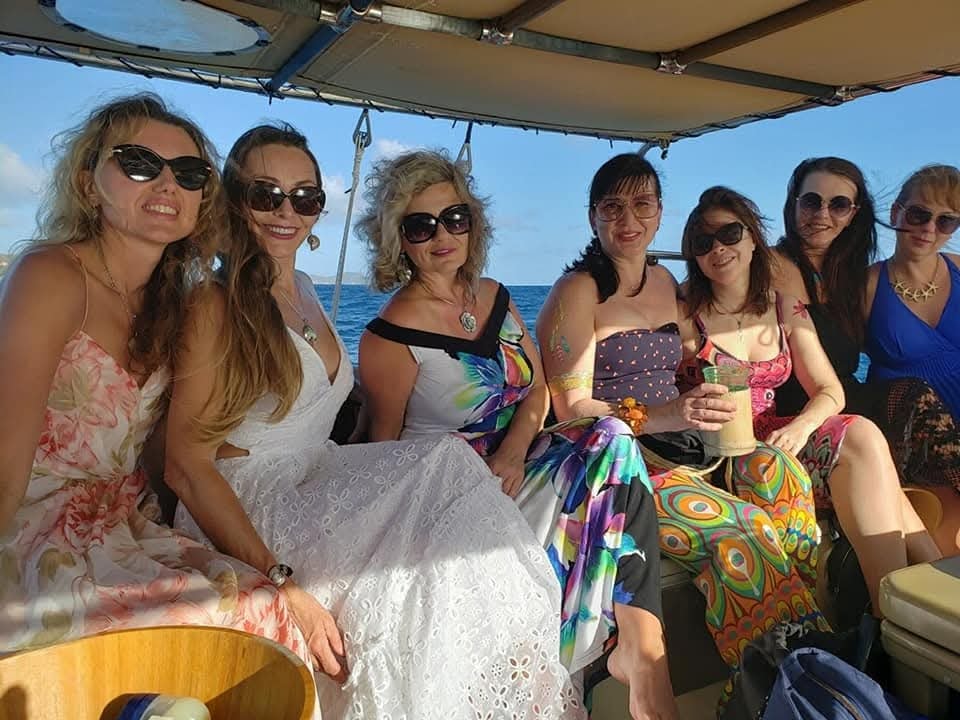 Group of women in colorful dresses smiling on charter under the bimini