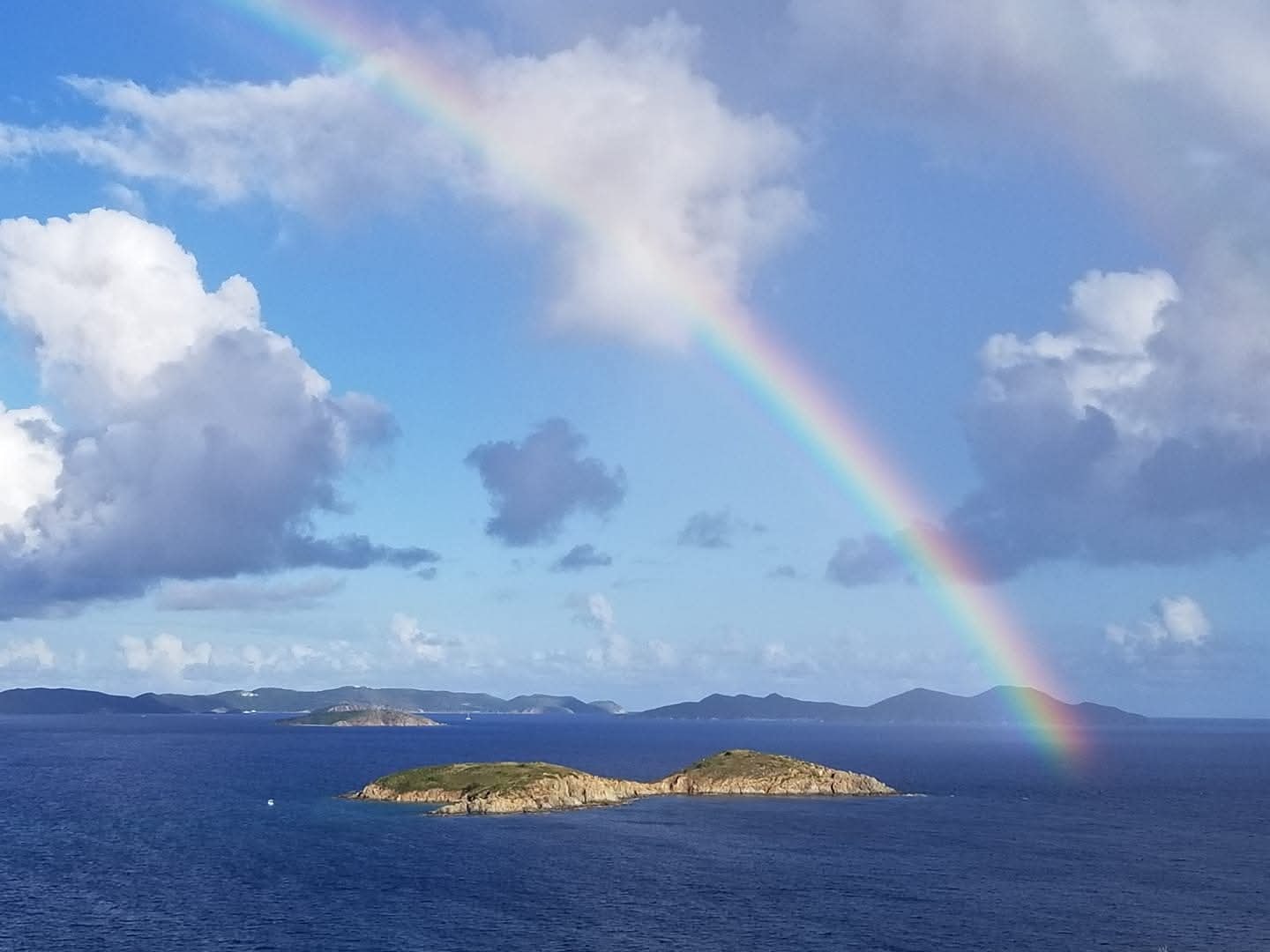 Full rainbow arc over open water and a small rocky Virgin Islands island