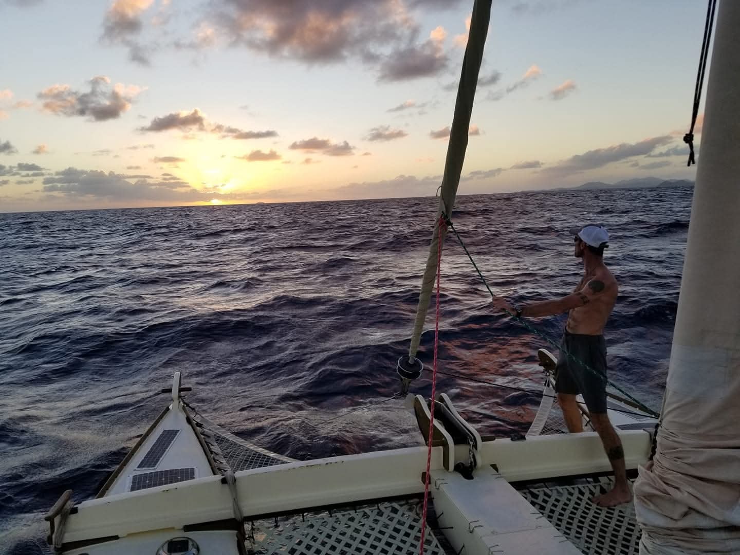 Captain working the lines at sunset on open ocean, white cap, VI islands on the horizon