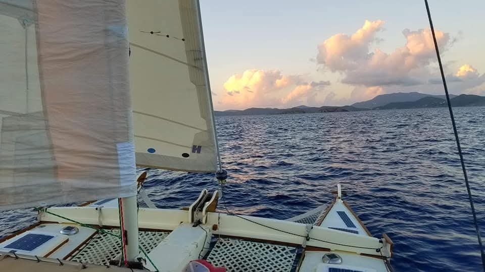 Mahiya deck at dusk with sails up, pink clouds, solar panels, and VI mountains