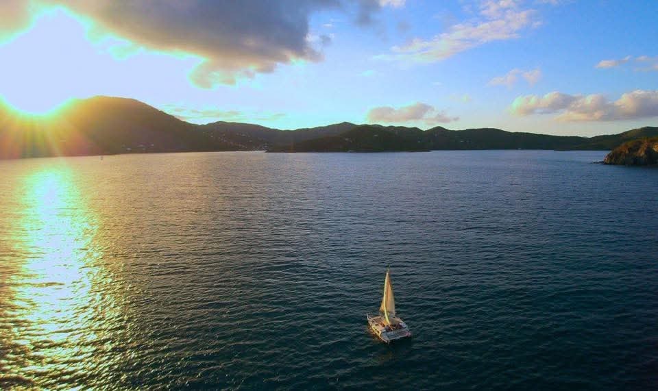Aerial drone shot of the Mahiya sailing in a golden VI bay at sunset, mountains silhouetted