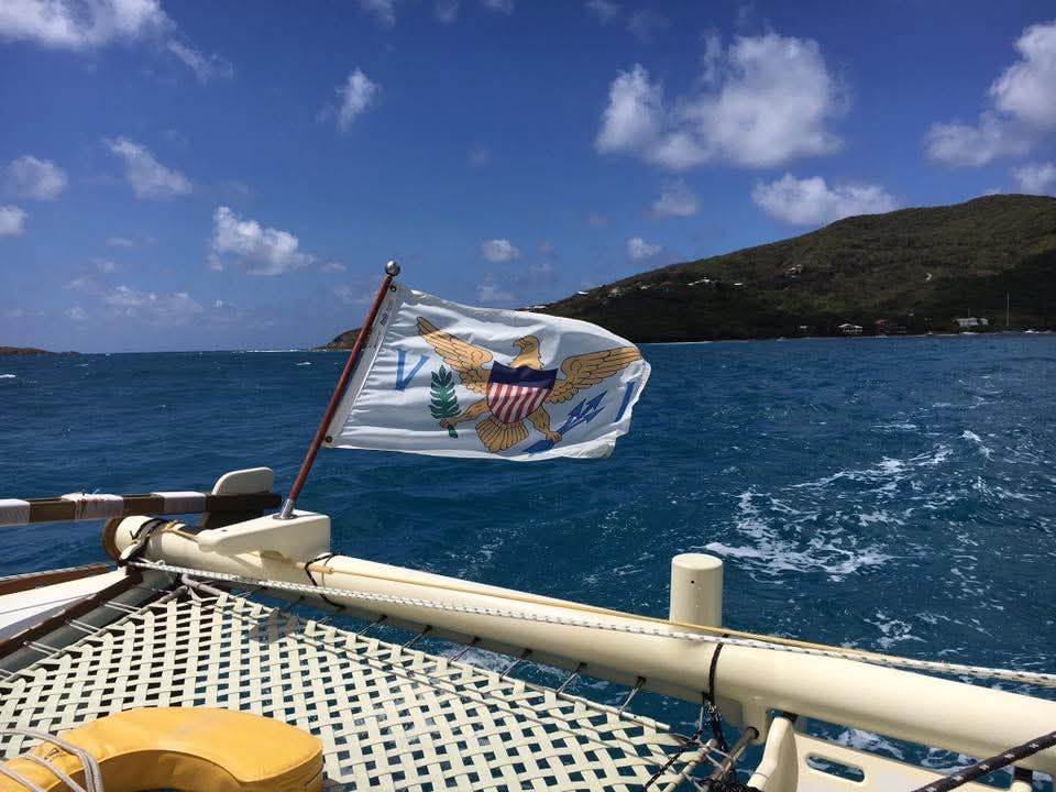 USVI flag flying proudly from the Mahiya bow with green VI hillside and harbor behind