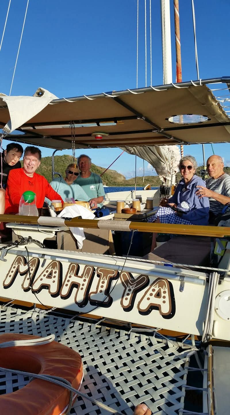 Happy group of guests aboard the Mahiya catamaran with the boat name clearly visible on the hull, VI hills behind