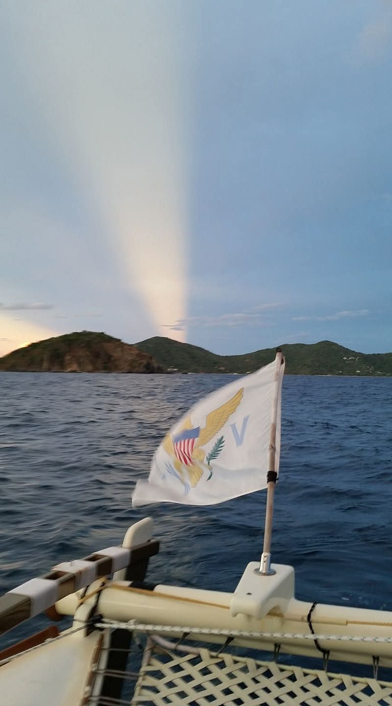 USVI flag flying from the Mahiya stern at dusk, a rainbow beam of light above VI mountains and dark blue water