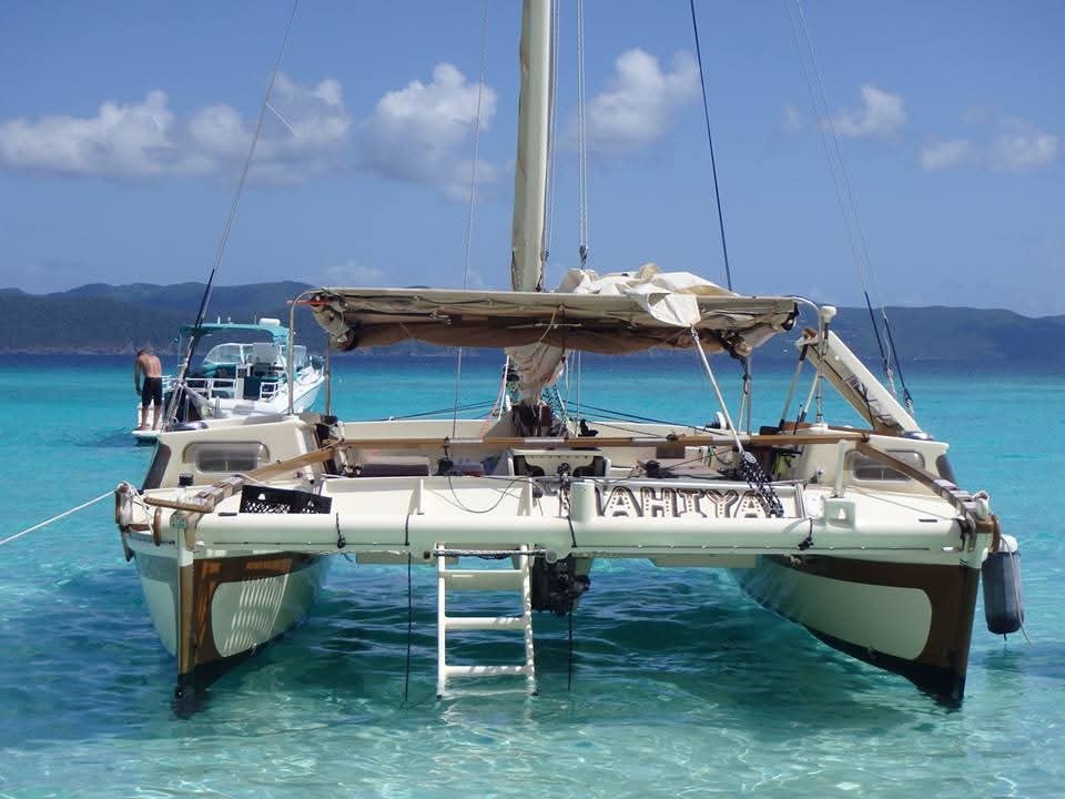 Mahiya catamaran anchored in brilliant crystal-clear turquoise water, MAHIYA name on hull, VI hillside behind