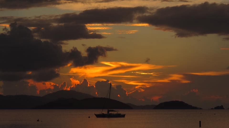 Dramatic fiery sunset with a sailboat silhouetted against glowing orange clouds and VI mountain islands