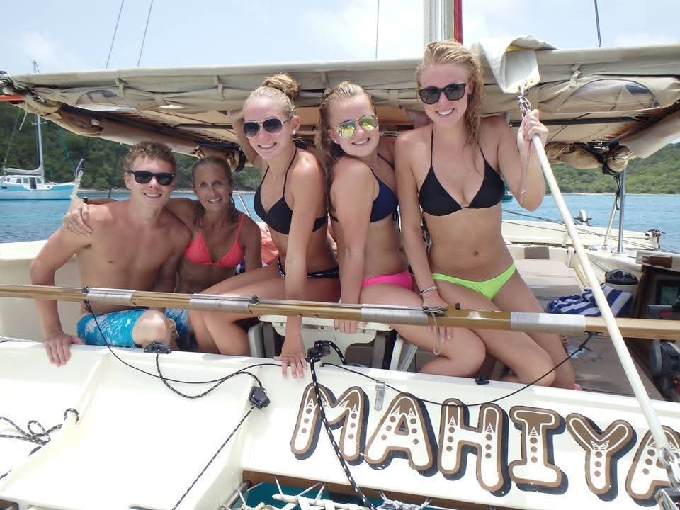Happy group of five young guests smiling aboard the Mahiya catamaran with MAHIYA name visible on the hull