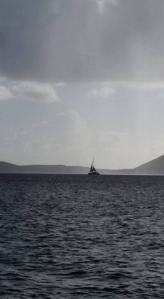 Mahiya catamaran silhouetted on moody dark blue water with VI mountains in the background under stormy skies