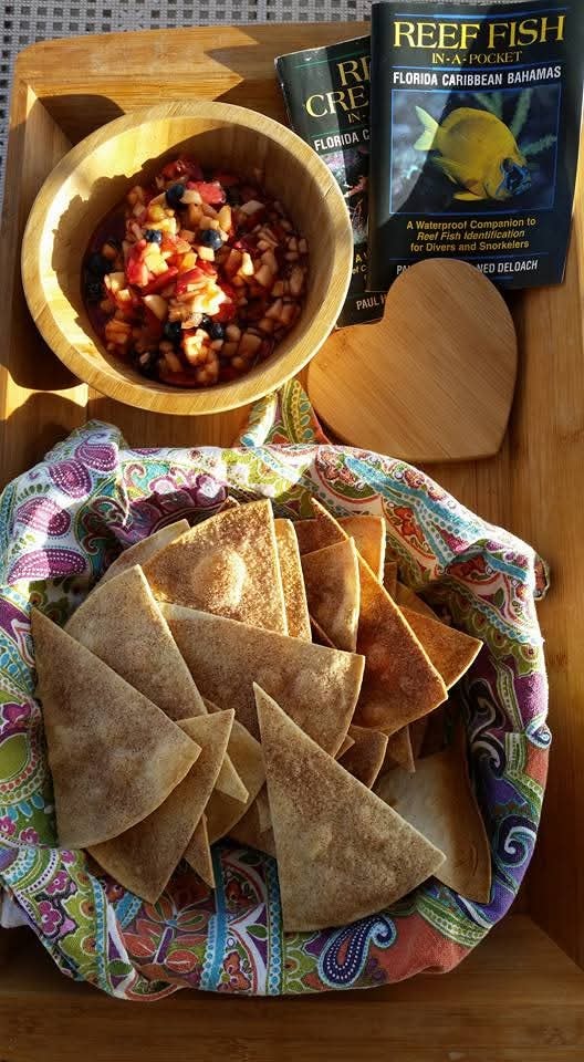 Black bean salsa in a wooden bowl with homemade tortilla chips on a colorful cloth, Reef Fish guide books alongside