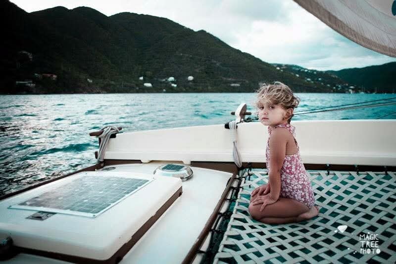 Young girl sitting on the Mahiya catamaran net at dusk, lush green VI mountains and turquoise water behind her