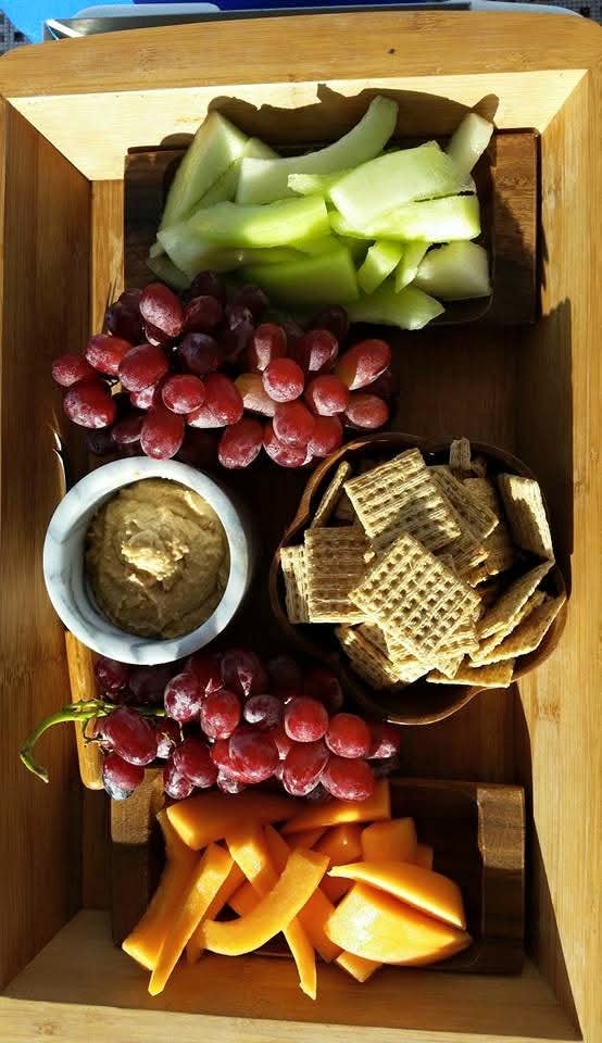 Charcuterie board with grapes, apple slices, hummus, crackers and carrots served on the Mahiya
