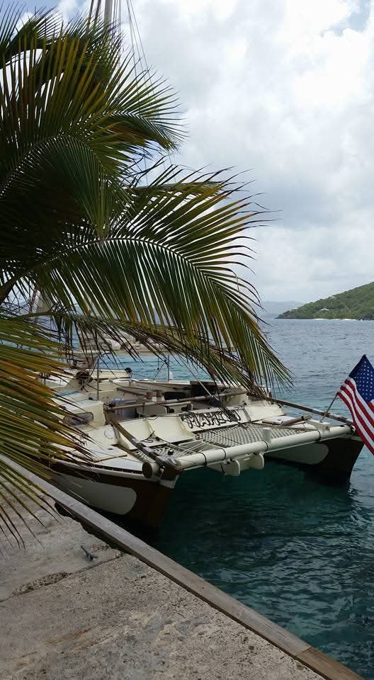 Mahiya catamaran docked at a tropical pier framed by palm fronds, American flag flying, lush VI hillside behind
