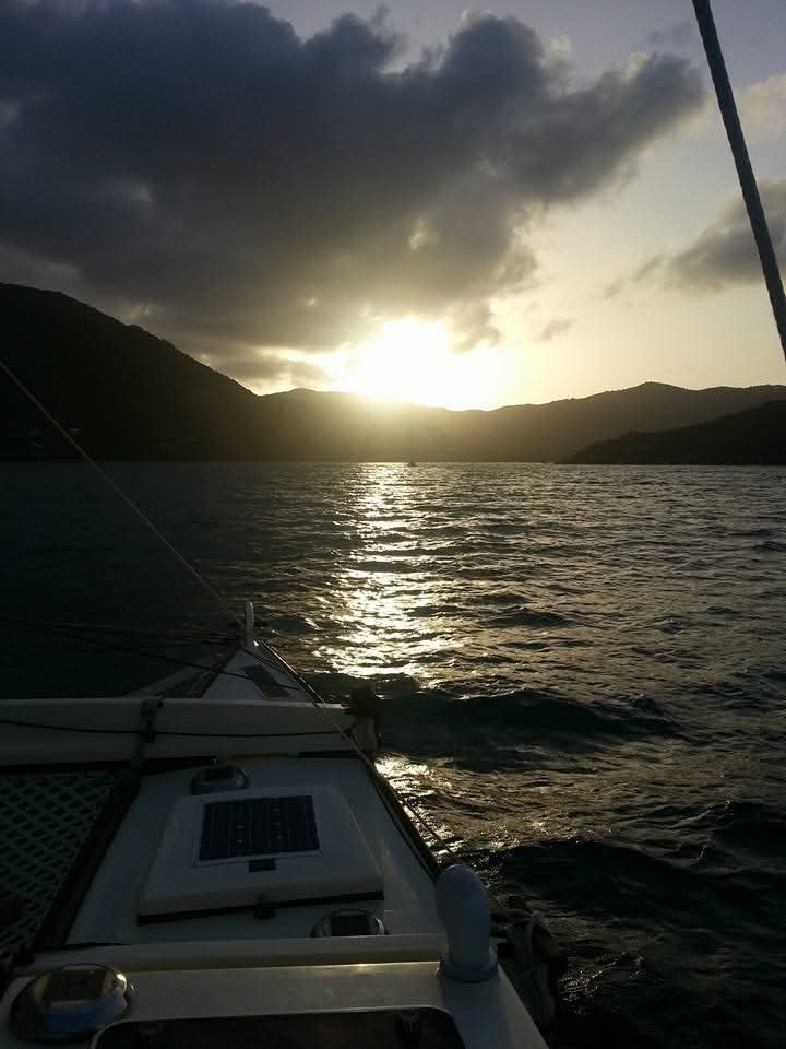 Dramatic golden sunset from the Mahiya deck, sun breaking through dark clouds over VI mountains, solar panel visible